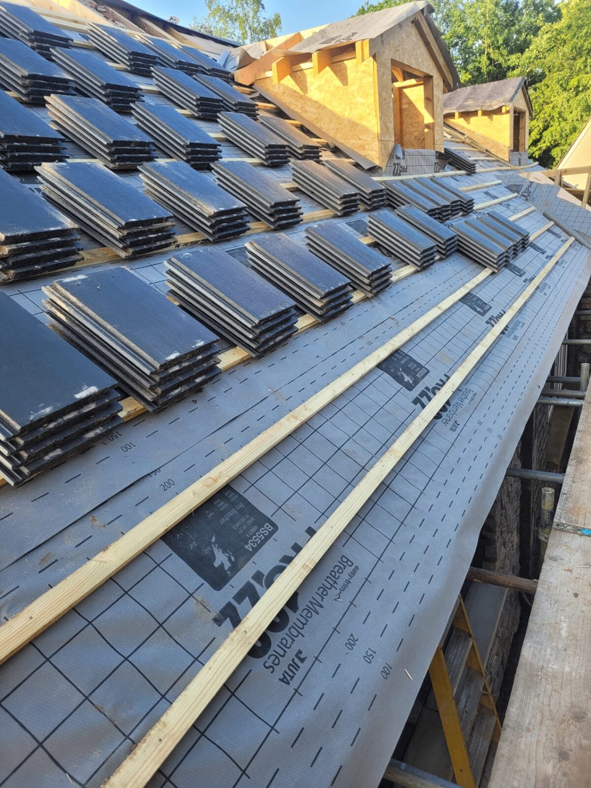 Slate tiles stacked on breather membrane mid-install